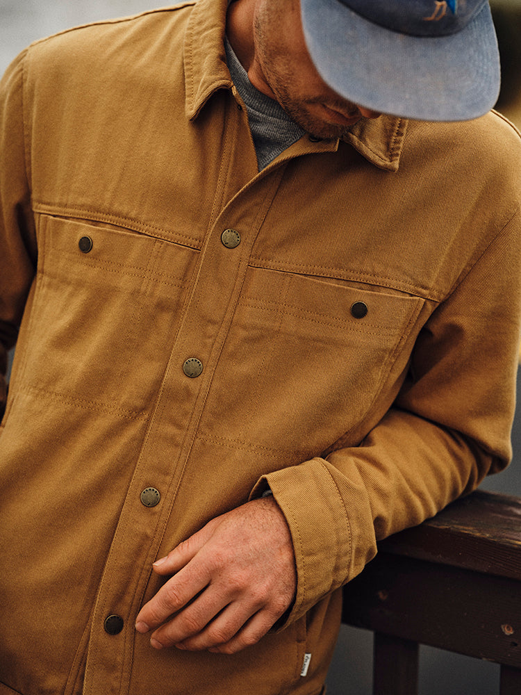 Man in a blue cap looks down, resting his arm on a railing, wearing a Pladra Men&