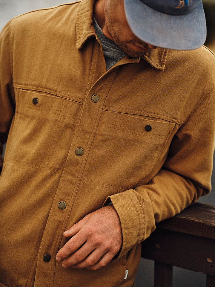 Man in a blue cap looks down, resting his arm on a railing, wearing a Pladra Men&