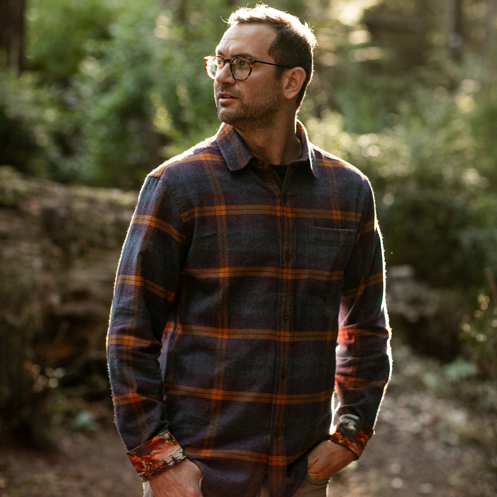 A man wears a Pladra Men's Every Day Flannel Shirt in Portsmouth Blue Heather, standing outdoors in sunlight.