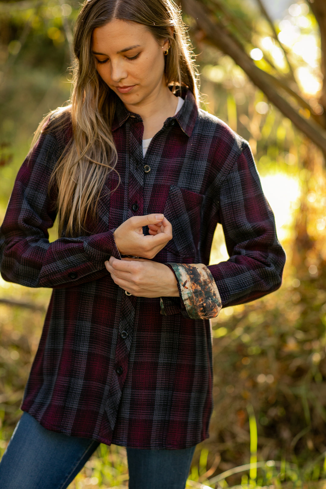 Outdoors in the sunlight, a woman adjusts the sleeve of her Women&