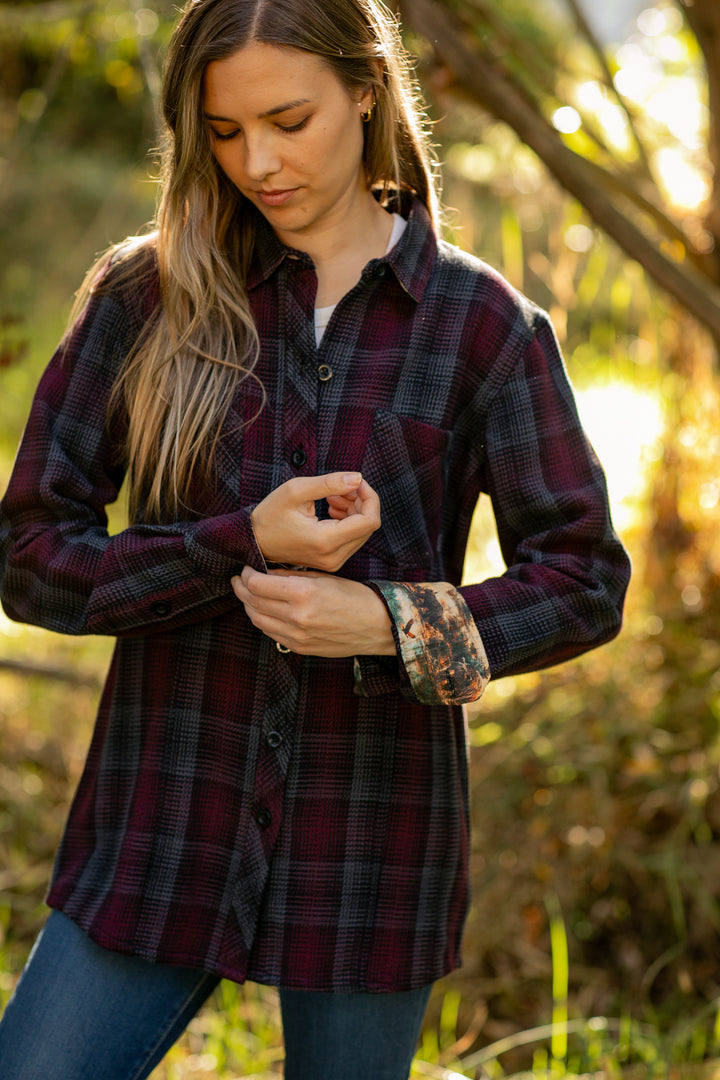 Outdoors in the sunlight, a woman adjusts the sleeve of her Women&