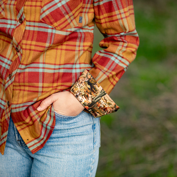 A woman outdoors stands in green grass, one hand in her pocket, wearing blue jeans and the Women&