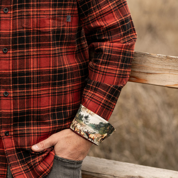 A person stands by a wooden fence with one hand in their pocket, wearing the Men&