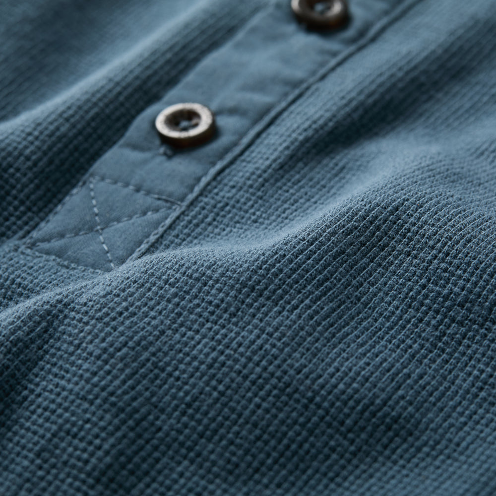 Close-up of the Men's Elko Henley in Atlantic Blue, featuring visible stitching, two brown buttons, and a cotton waffle weave for a soft, textured look with classic fit.