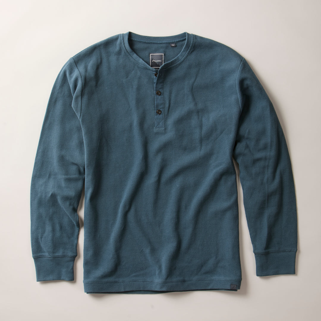 The Men's Elko Henley in Atlantic Blue, a cotton waffle classic fit shirt with long sleeves and three collar buttons, is laid flat on a light surface. It features a textured fabric and a simple, relaxed design.