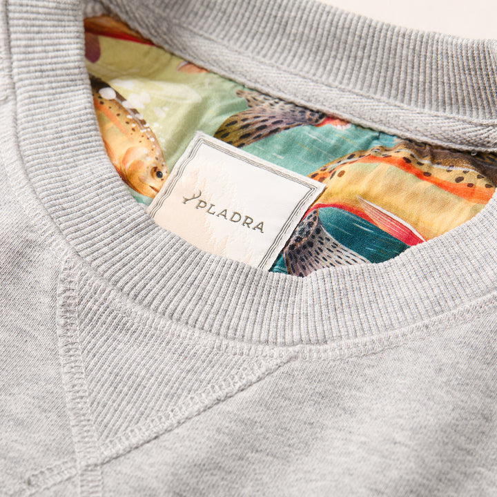 Close-up of the Men's Klamath Crew in Fog Grey, featuring a PLADRA label on the collar. The French terry interior showcases a vibrant fish pattern with greens, oranges, and detailed scales.