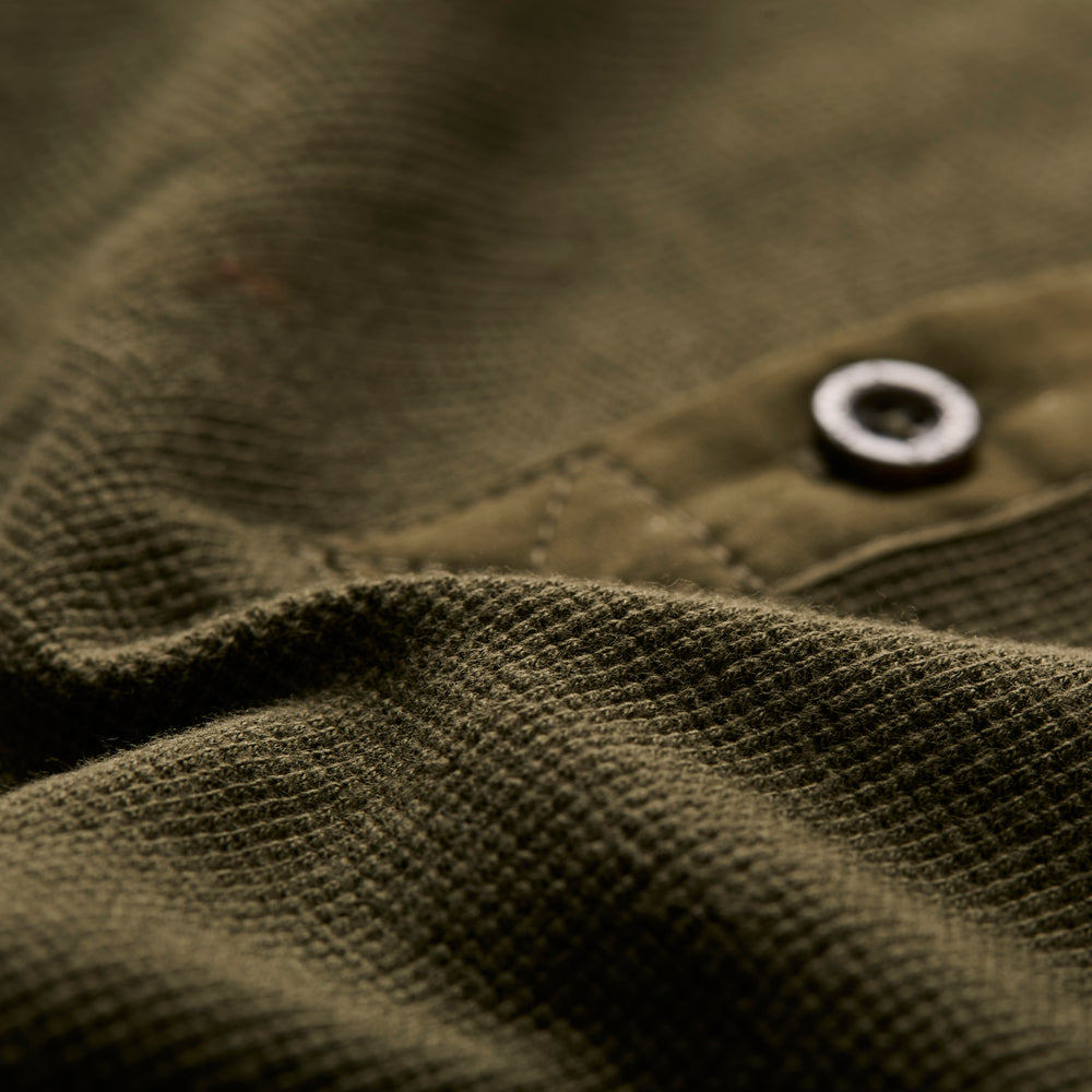 Close-up of forest green textured fabric from the Women's Elko Henley, featuring a visible seam and black button. Lighting accentuates the weave pattern and soft folds of this mid-weight material.