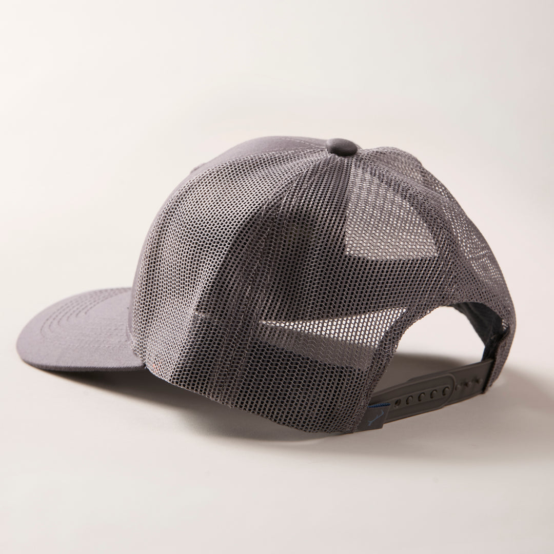 The Mountain Trucker Hat- Charcoal Grey is displayed from the back and side, featuring breathable mesh and an adjustable snapback strap against a light background.