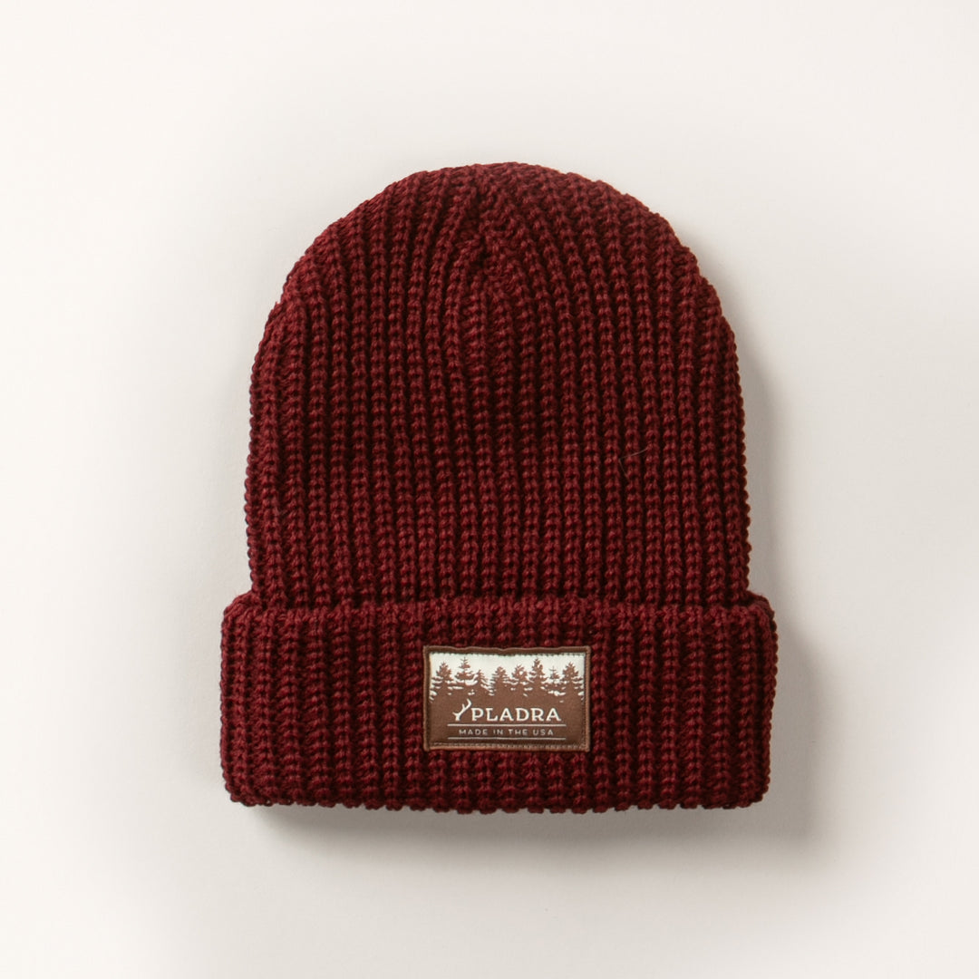 The Woodsman Heavyweight Cuff Beanie in Burgundy Red is made in the USA, features a folded brim with a rectangular patch label of trees and PELADRA text on the front, and is shown on a plain white background.