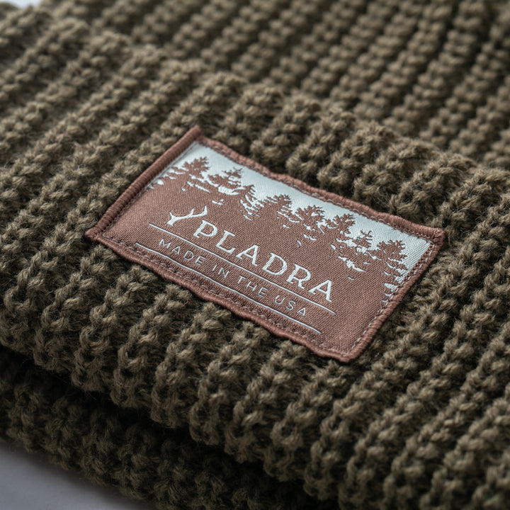 Close-up of Pladra Woodsman Heavyweight Cuff Beanie in olive green with tree patch and "Made in the USA" text.
