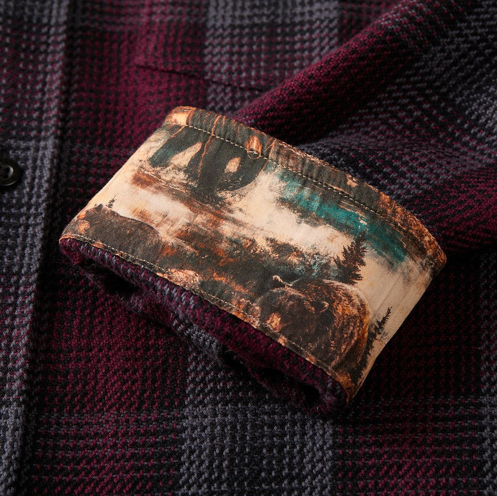 A close-up of the Women's Fireside Flannel in Hickory Red, showing its heavyweight maroon and black sleeve with cuff turned up to reveal an inner lining printed with bears, trees, and mountains in earthy colors.