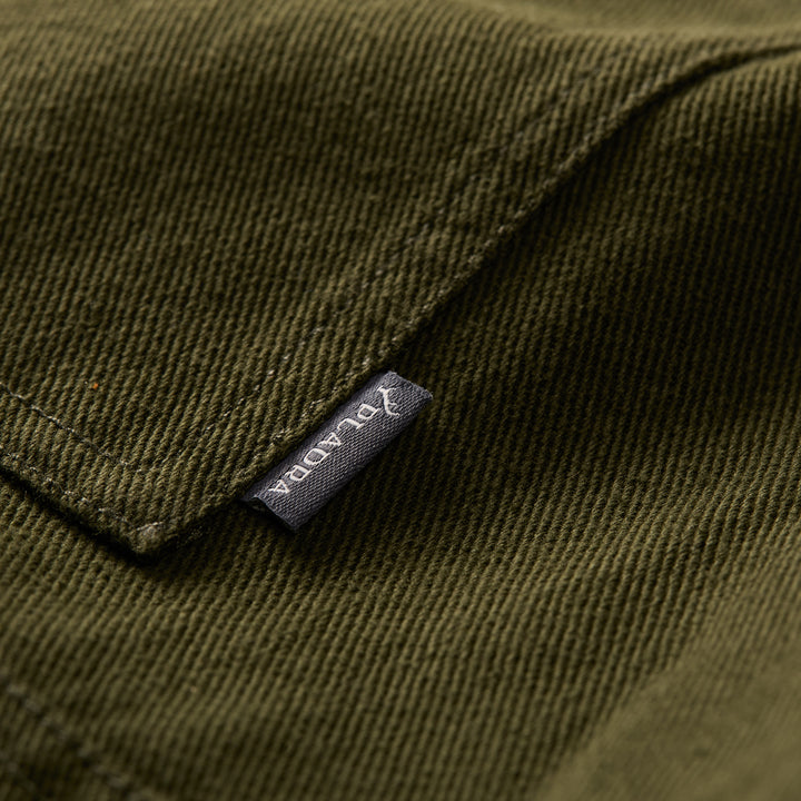 Close-up of hunter green cotton fabric with a visible seam and a small black Pladra tag on the Men&