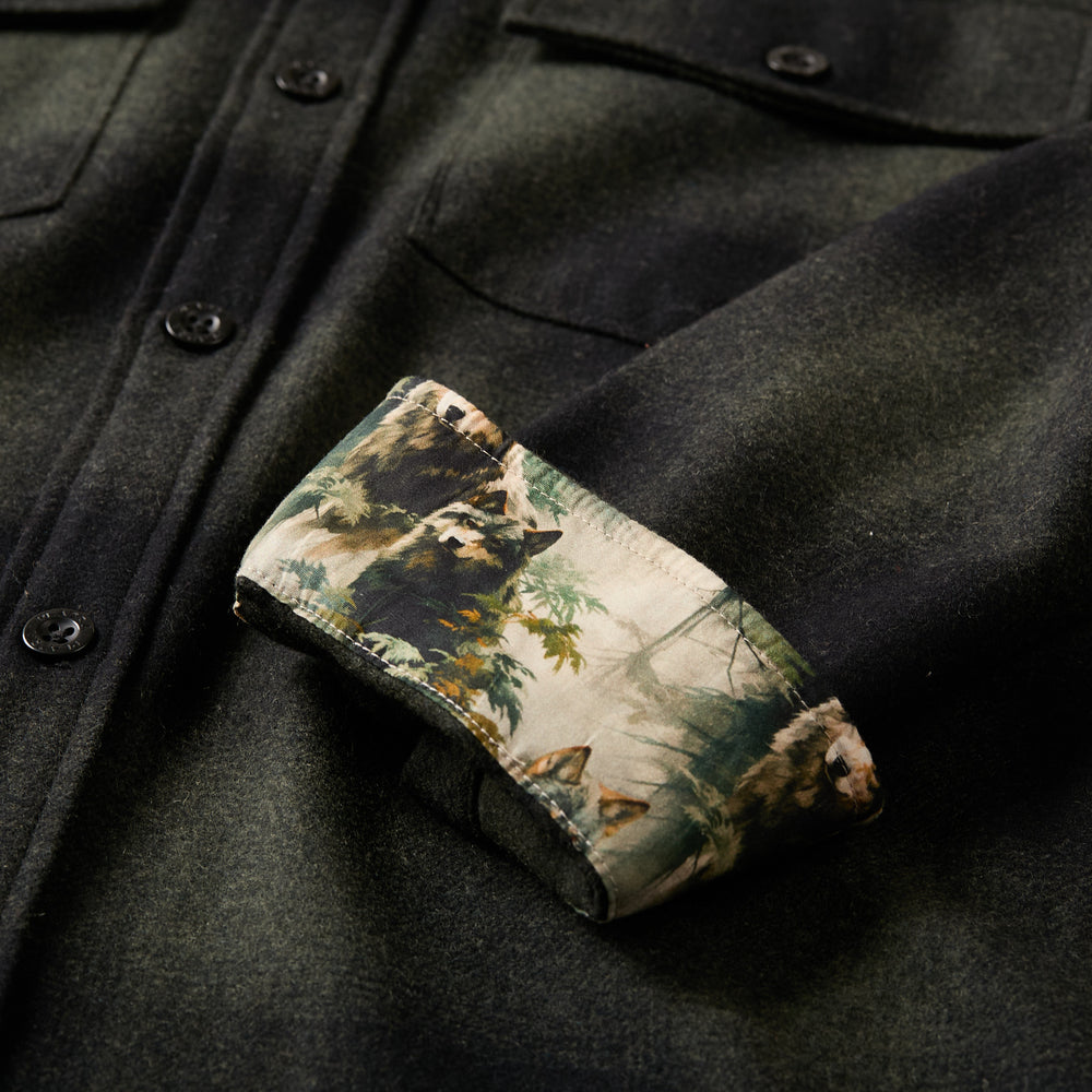 A close-up of the Men's Workhorse Wool Flannel Shirt in Moss Green shows a rolled sleeve, revealing its illustrated forest and bear scene lining.
