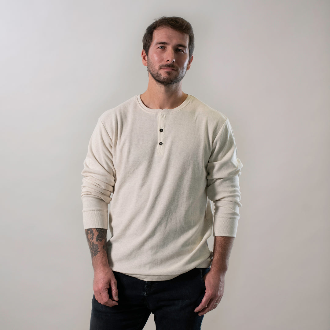 A man with short brown hair and a beard stands against a plain light background, wearing the Men&