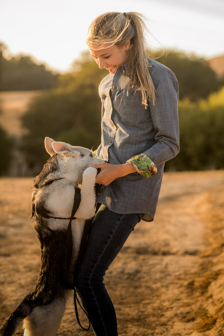 A young woman smiles outdoors as a large dog stands on its hind legs, paws on her waist. She wears the Women&