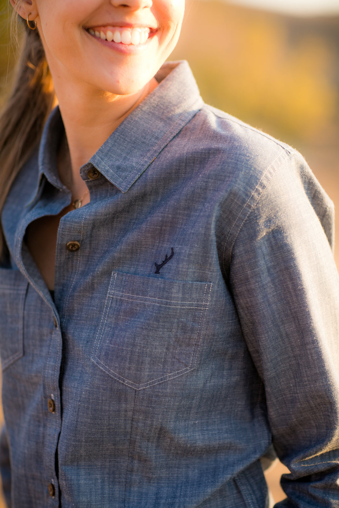 A smiling woman stands outdoors in warm sunlight wearing the Women&