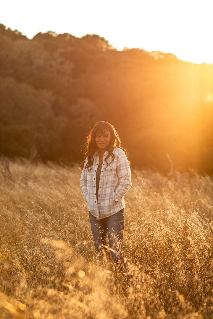 A woman stands in a sunlit field wearing the Pladra Women&