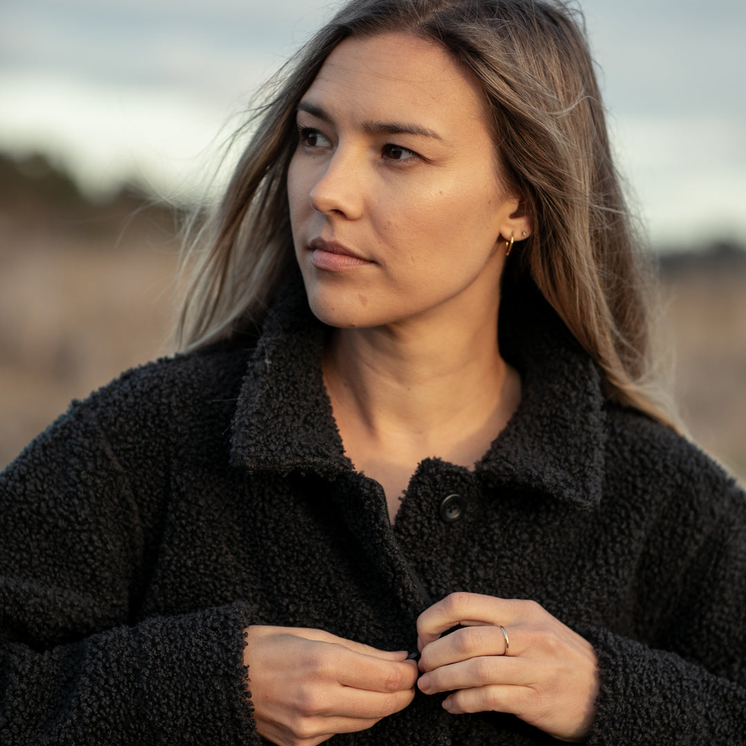 A woman with long, light brown hair stands outdoors, fastening her Women&
