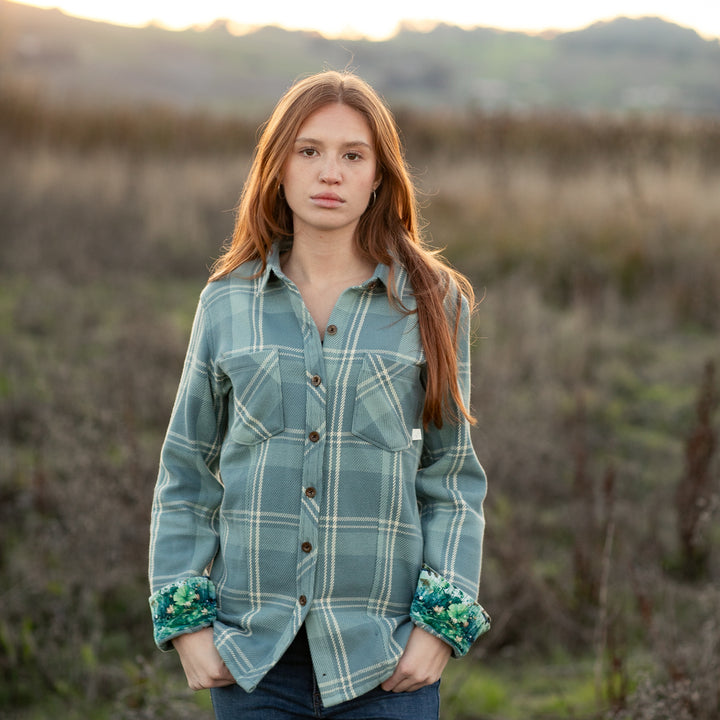 A young woman with long red hair stands in a field, wearing the Women&