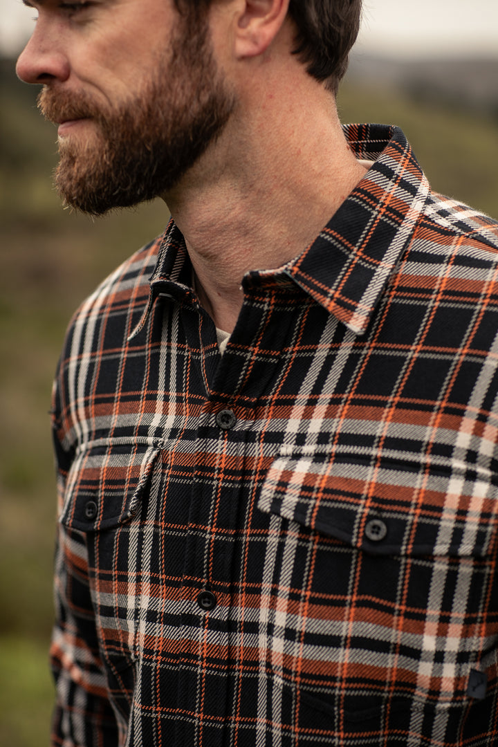 A man outdoors in a Pladra Men’s Workhorse Elite Flannel Shirt–Posey Black, classic and rugged, face partly out of frame.