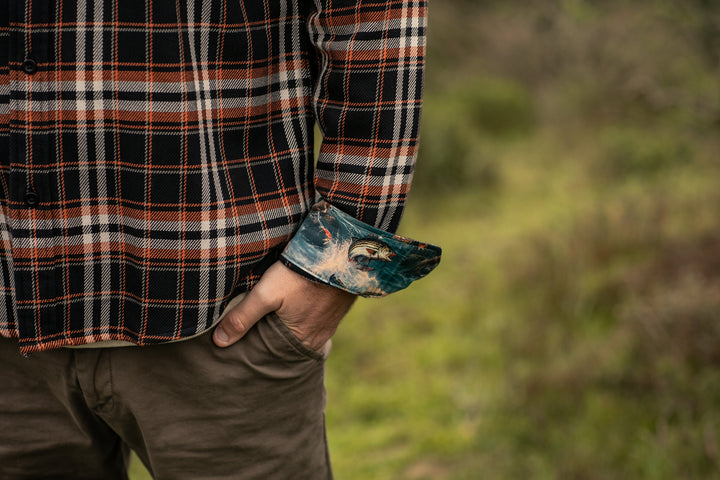 A man wears the Pladra Men’s Workhorse Elite Flannel Shirt in Posey Black, outdoors with a hand in his pocket.
