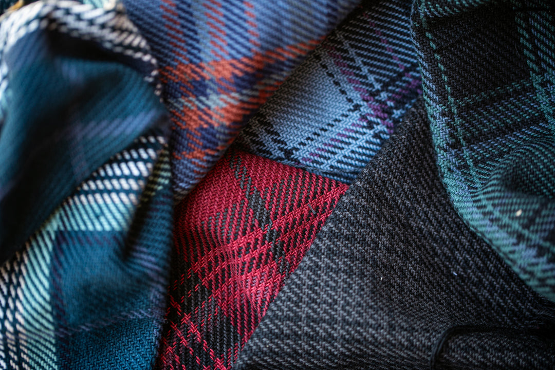 A close-up of various colorful plaid fabrics layered together, including red, blue, green, and black patterns.