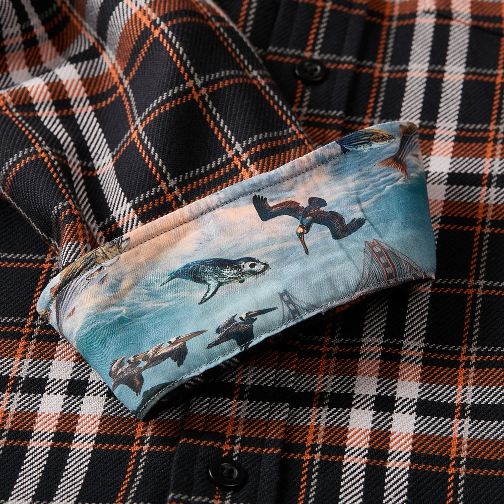 The Men's Workhorse Elite Flannel Shirt - Posey Black is a black, orange, and white Portuguese flannel shirt with turned-up cuffs showcasing a vibrant print of birds, a sea turtle, waves, and bridge structures.
