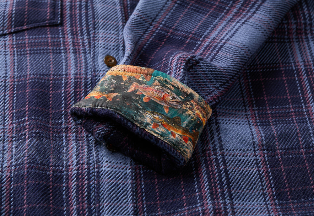 The Men's Fireside Flannel - Riffle Blue by Pladra features blue plaid and trout-patterned cuffs in soft organic cotton.