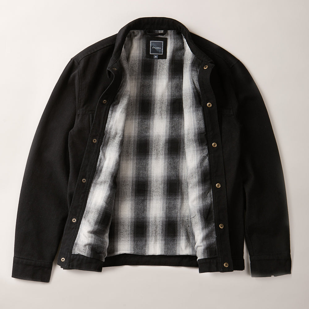 The Men's Sequoia Jacket in Shadow Black is displayed flat and open, showing its black, white, and gray plaid flannel lining against a neutral background.