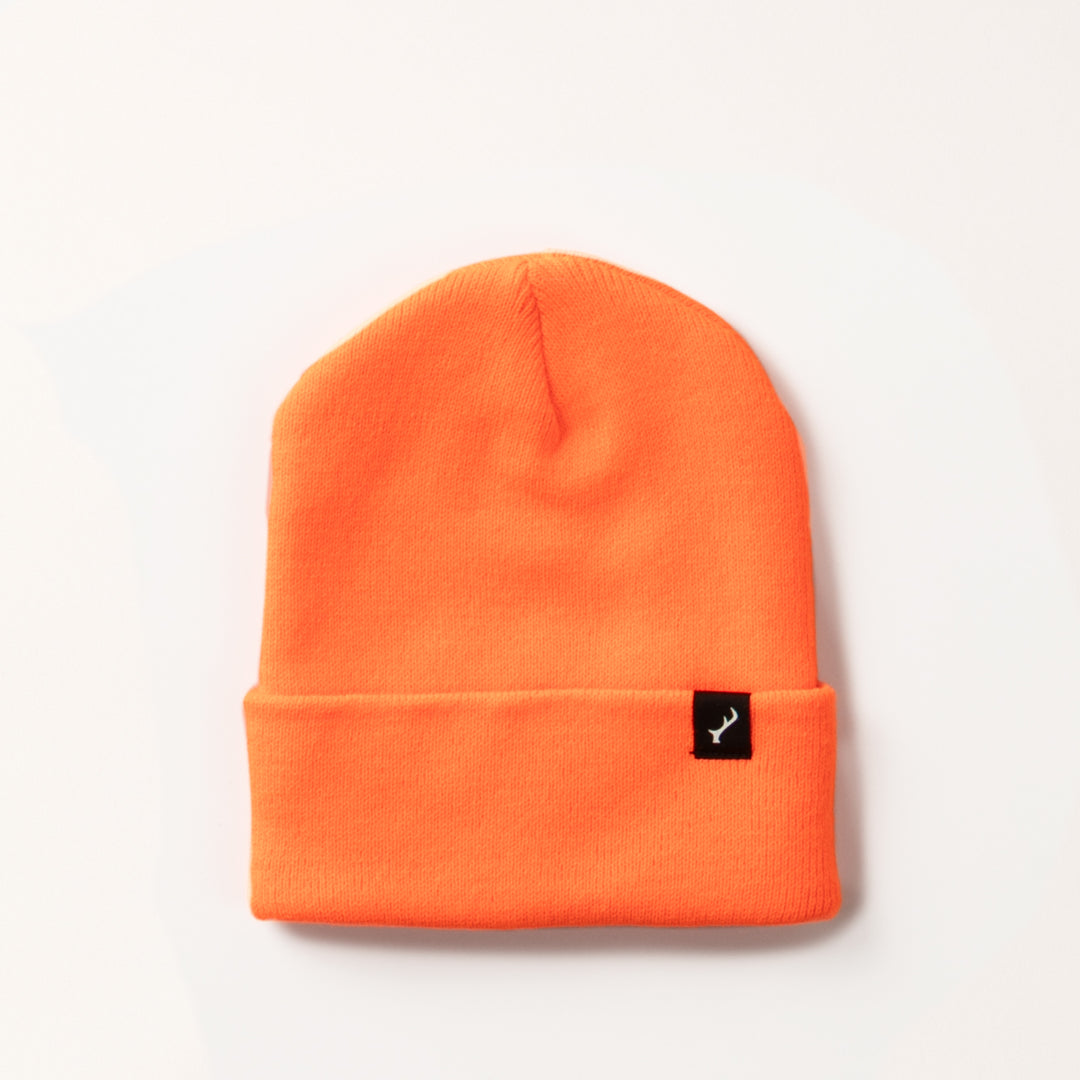 The Stretch Cuff Beanie- Hunter Orange is a vibrant acrylic beanie with a folded brim and a small black tag featuring a white logo on the front, displayed against a plain light background.