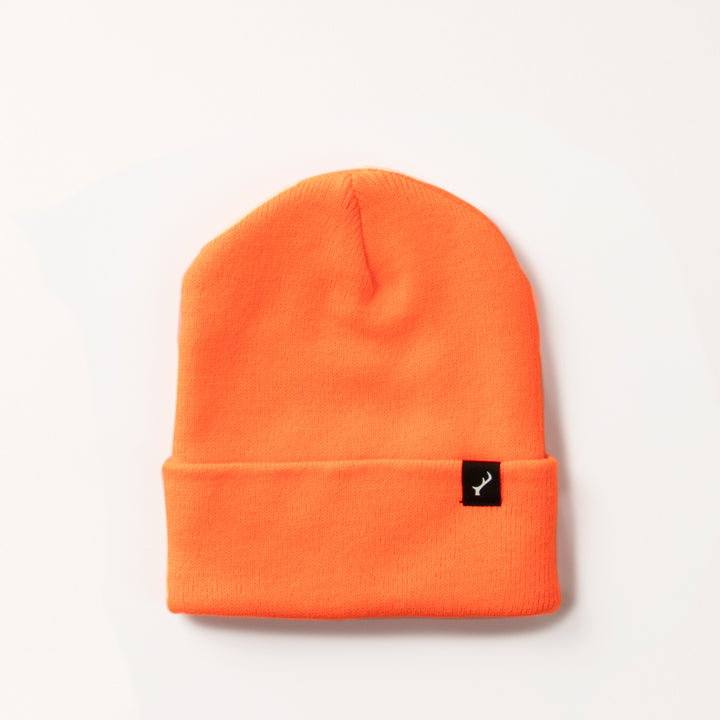 The Stretch Cuff Beanie- Hunter Orange is a vibrant acrylic beanie with a folded brim and a small black tag featuring a white logo on the front, displayed against a plain light background.