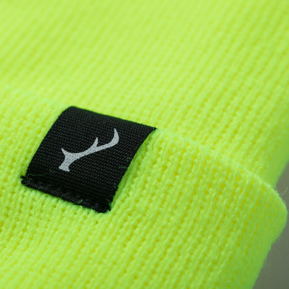 Close-up of Pladra Stretch Cuff Beanie in Safety Yellow, black tag, antler symbol, made in USA.