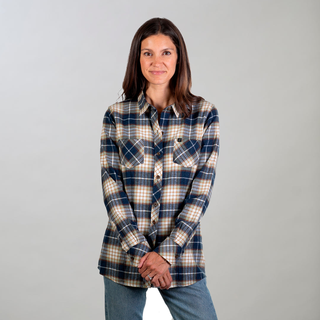 A woman with straight brown hair stands against a light background, wearing the Women's Every Day Flannel Shirt- Banff Blue and blue jeans, hands clasped in front of her and smiling slightly.