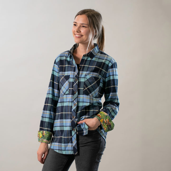 A woman with long hair tied back is smiling against a plain background, wearing the Women&
