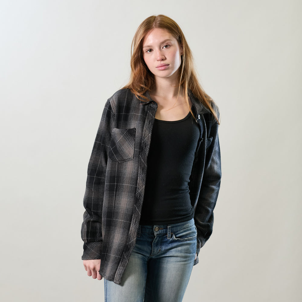Young woman in Pladra Women's Fireside Flannel - Cast Iron Black, jeans, and loose brown hair stands against a plain backdrop.