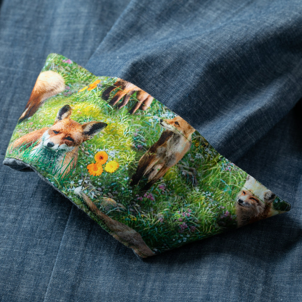 The Women's Cascade Shirt in Indigo Blue Chambray features turned-up sleeves that reveal vibrant foxes in a green meadow with flowers on the inner cuffs—a striking, sustainable cotton detail for an outdoor look.