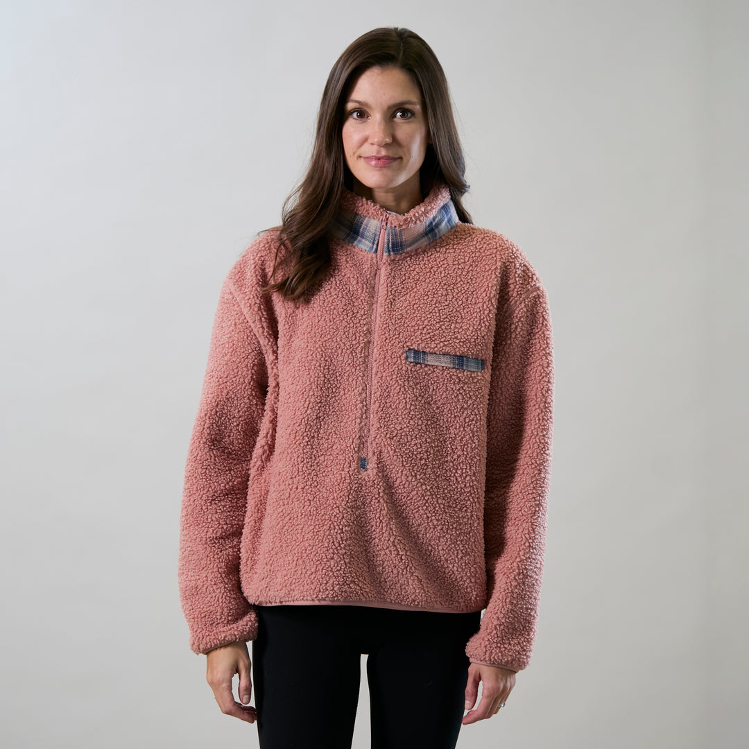 A woman with long brown hair wears a Women's Jenner Sherpa Fleece in coral pink over black leggings, standing against a plain light background and smiling slightly.