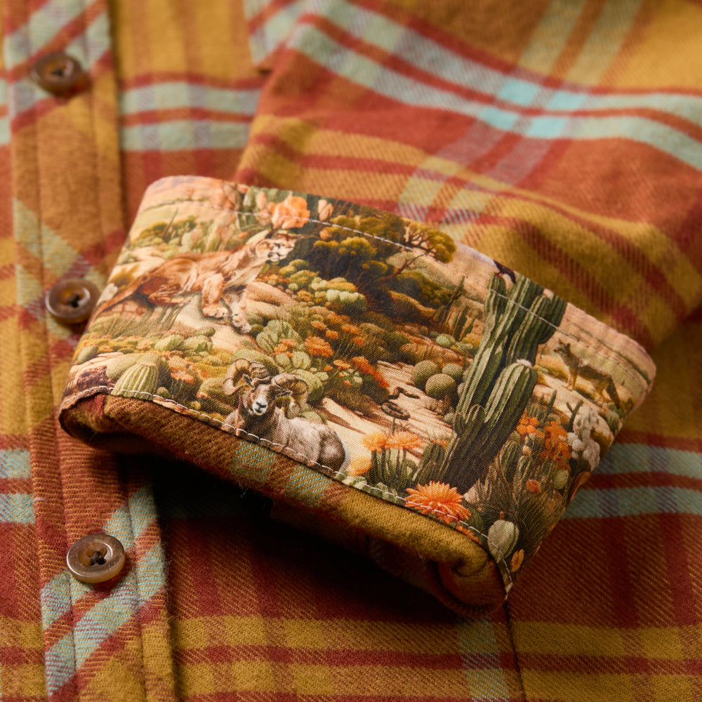 Close-up of the Women's Every Day Flannel Shirt–Cottonwood Orange in warm plaid, crafted from premium Portuguese cotton flannel. A turned-up cuff reveals a colorful desert scene lining, accented by brown buttons.