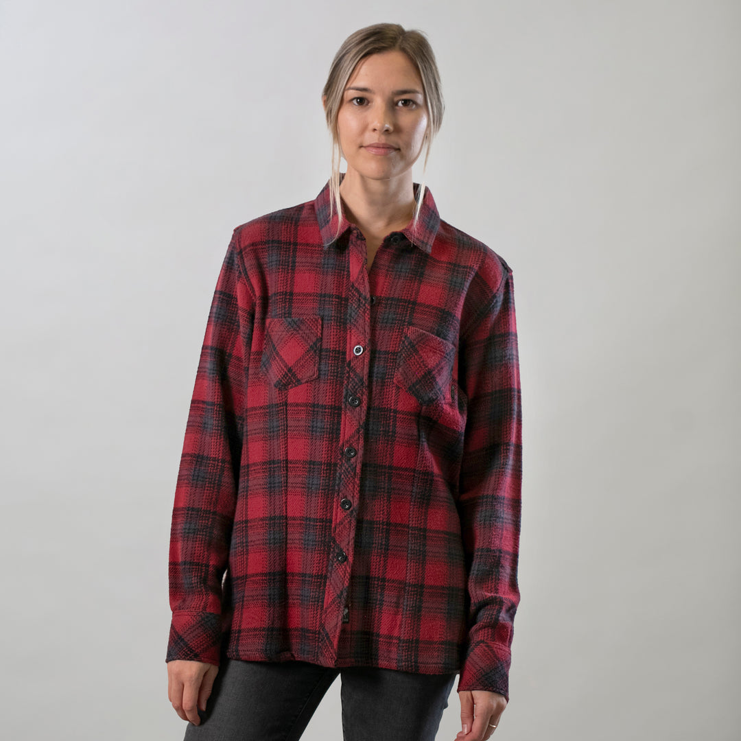 A woman with light brown hair wears the Women's Fireside Flannel in Deadwood Red and dark pants, standing against a light gray background and looking at the camera with a neutral expression.