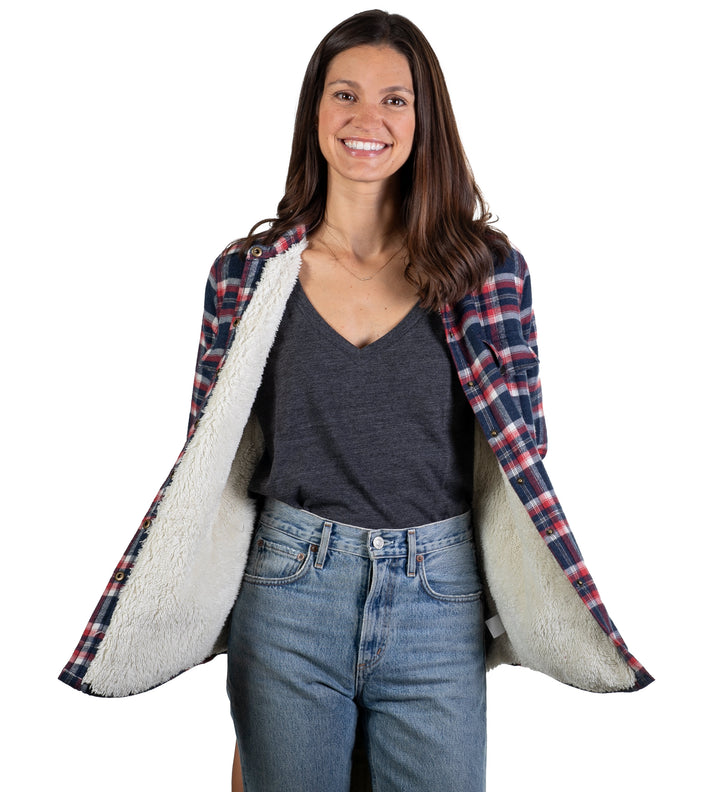 A smiling woman in a gray V-neck and blue jeans holds open the Women&