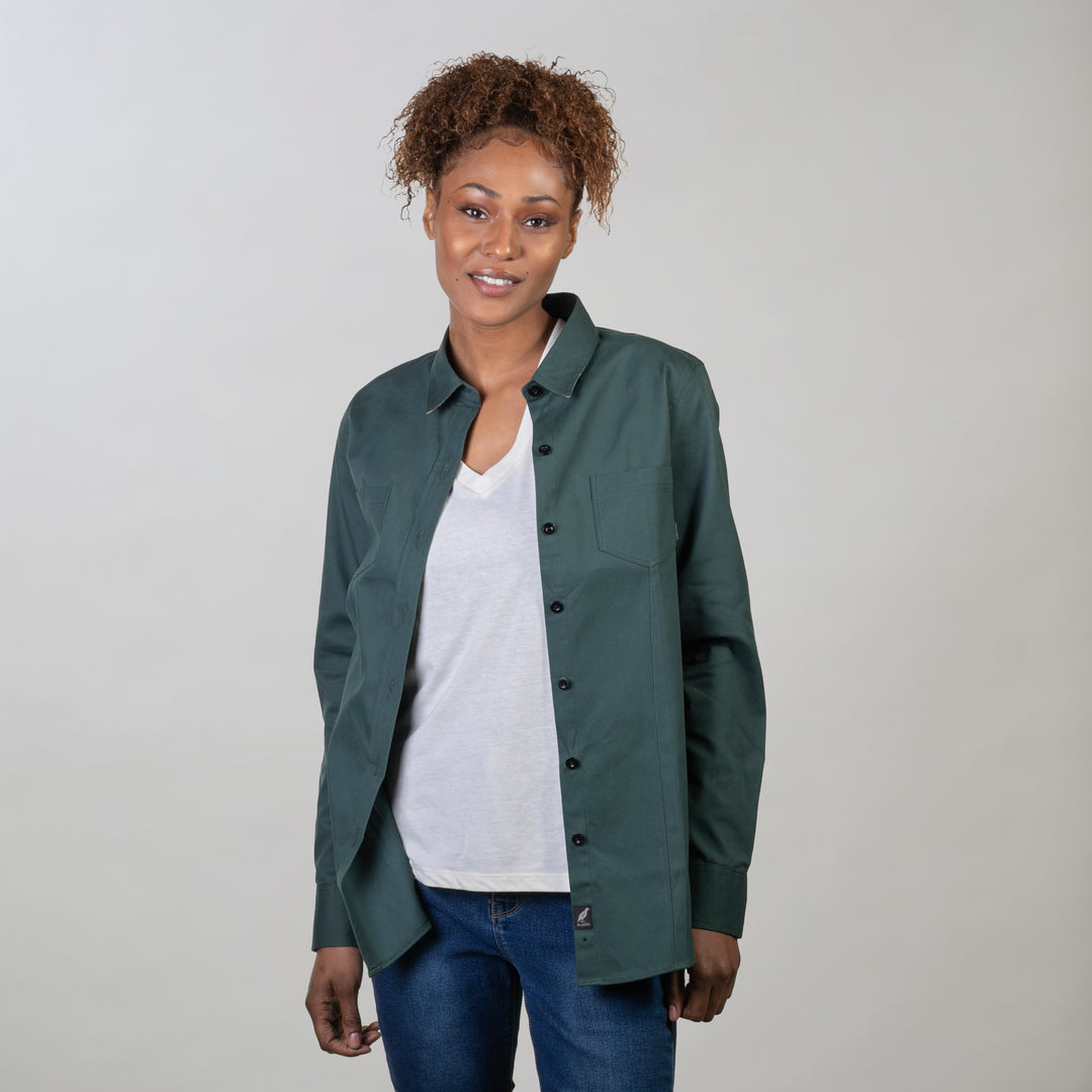 Woman in Pladra Women's Leon Workhorse Shirt–Fir Green Pincord over a white tee and jeans, smiling against a plain background.