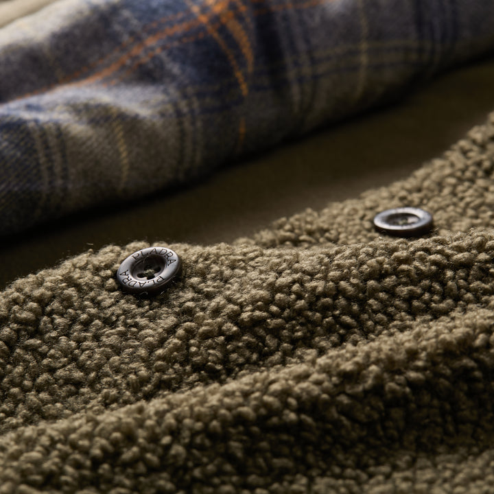 Close-up of Pladra Women's Headlands Sherpa Shacket in Forest Green, featuring black snaps and plaid flannel lining.