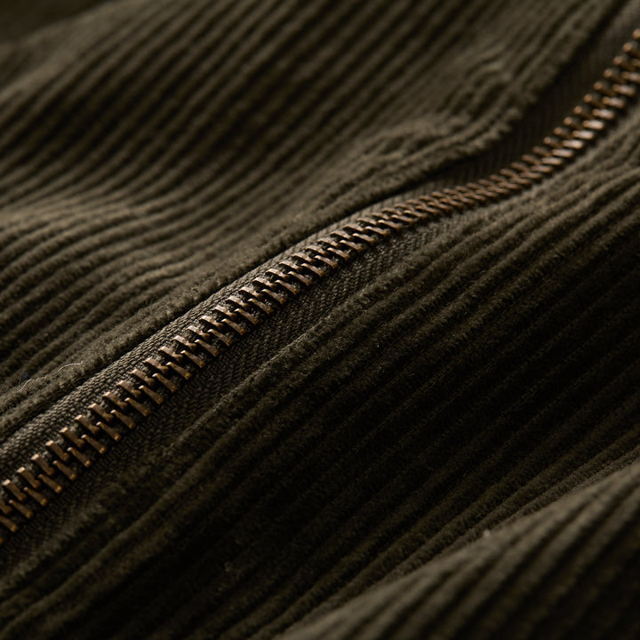 Close-up of a brown metal zipper on dark corduroy fabric, highlighting the ridges and zipper details on the Women&