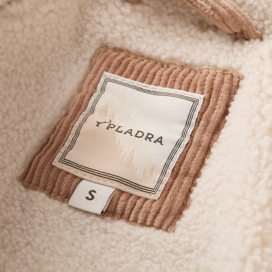 A close-up of a Pladra S tag on the Women’s Stinson Jacket in Oak Tan, featuring cream fleece and corduroy patch.
