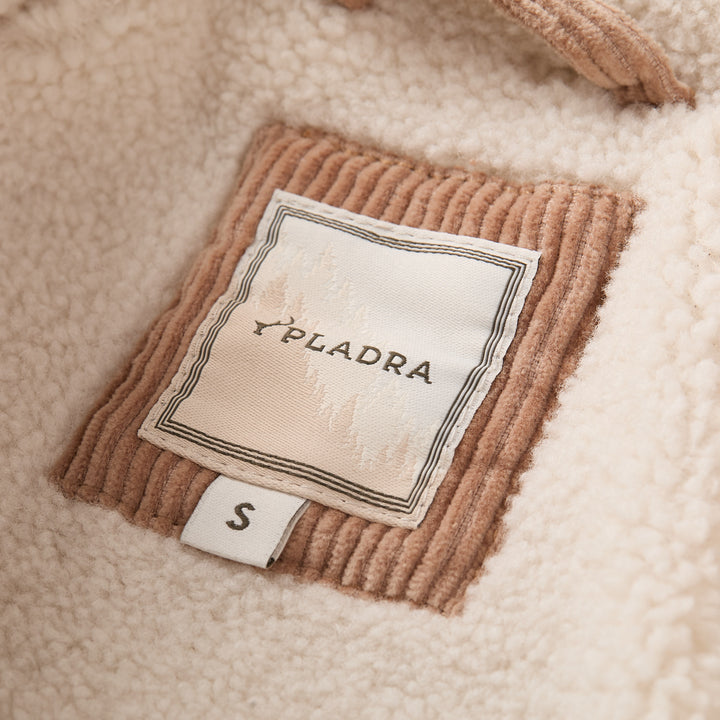A close-up of a Pladra S tag on the Women’s Stinson Jacket in Oak Tan, featuring cream fleece and corduroy patch.