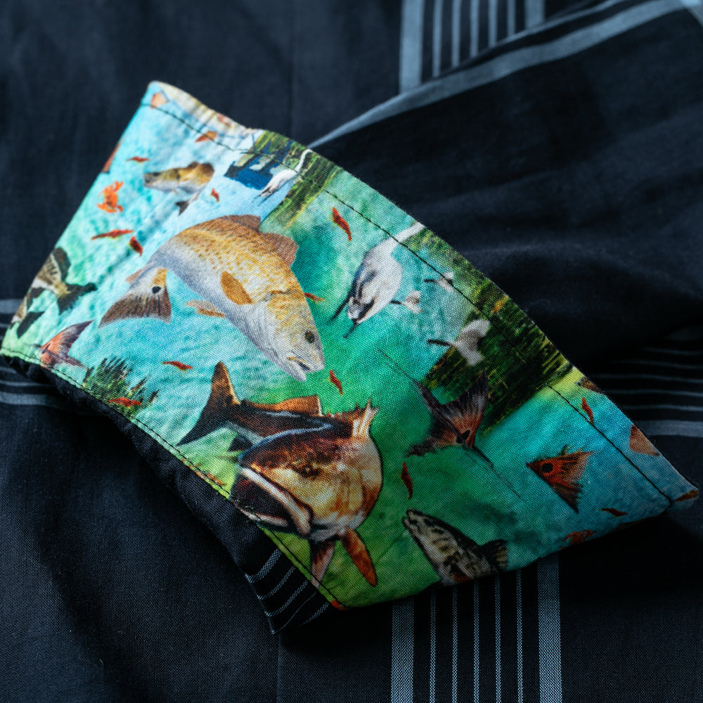 A close-up of the Women's Breeze Shirt- Ocean Blue shows a tencel cotton sleeve with a vibrant fish-print cuff on a blue-green background, contrasting with the dark shirt's thin white stripes.