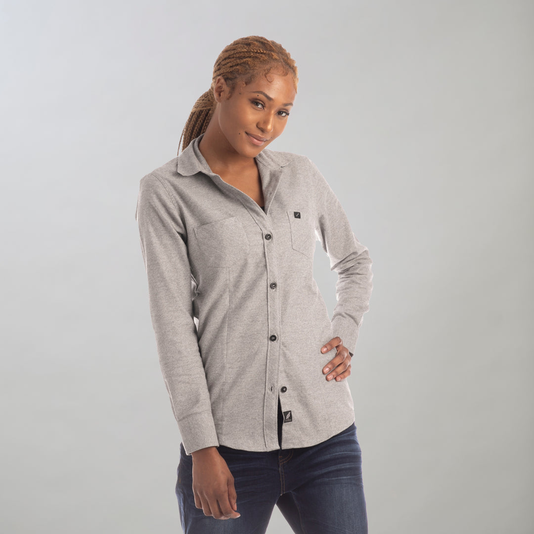 A woman with braided hair models the Women's Cascade Flannel Shirt in Stratus Grey, paired with dark jeans. She stands against a plain light background, one hand on her hip and the other relaxed by her side.