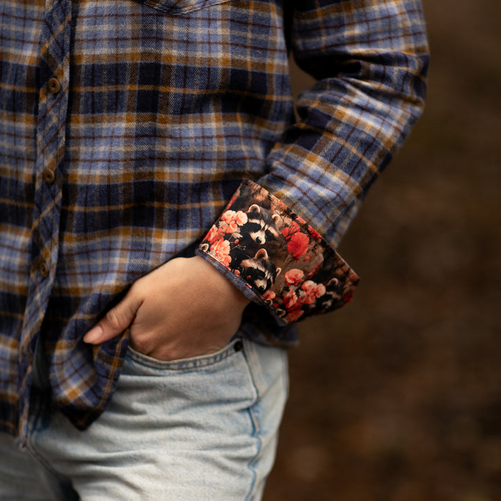 Person wearing a plaid shirt with floral cuffs and jeans against a blurred background