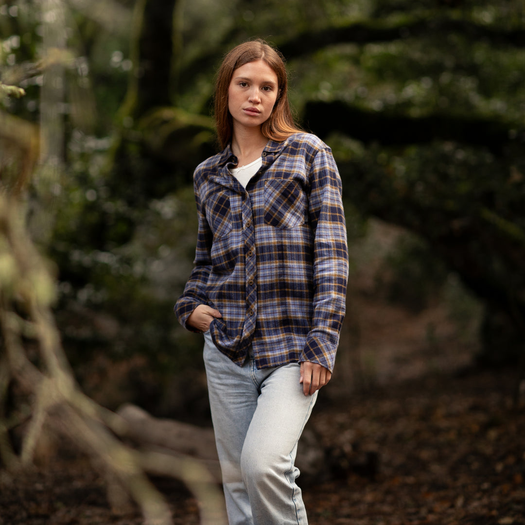 Woman wearing a plaid shirt and jeans standing in a forest setting
