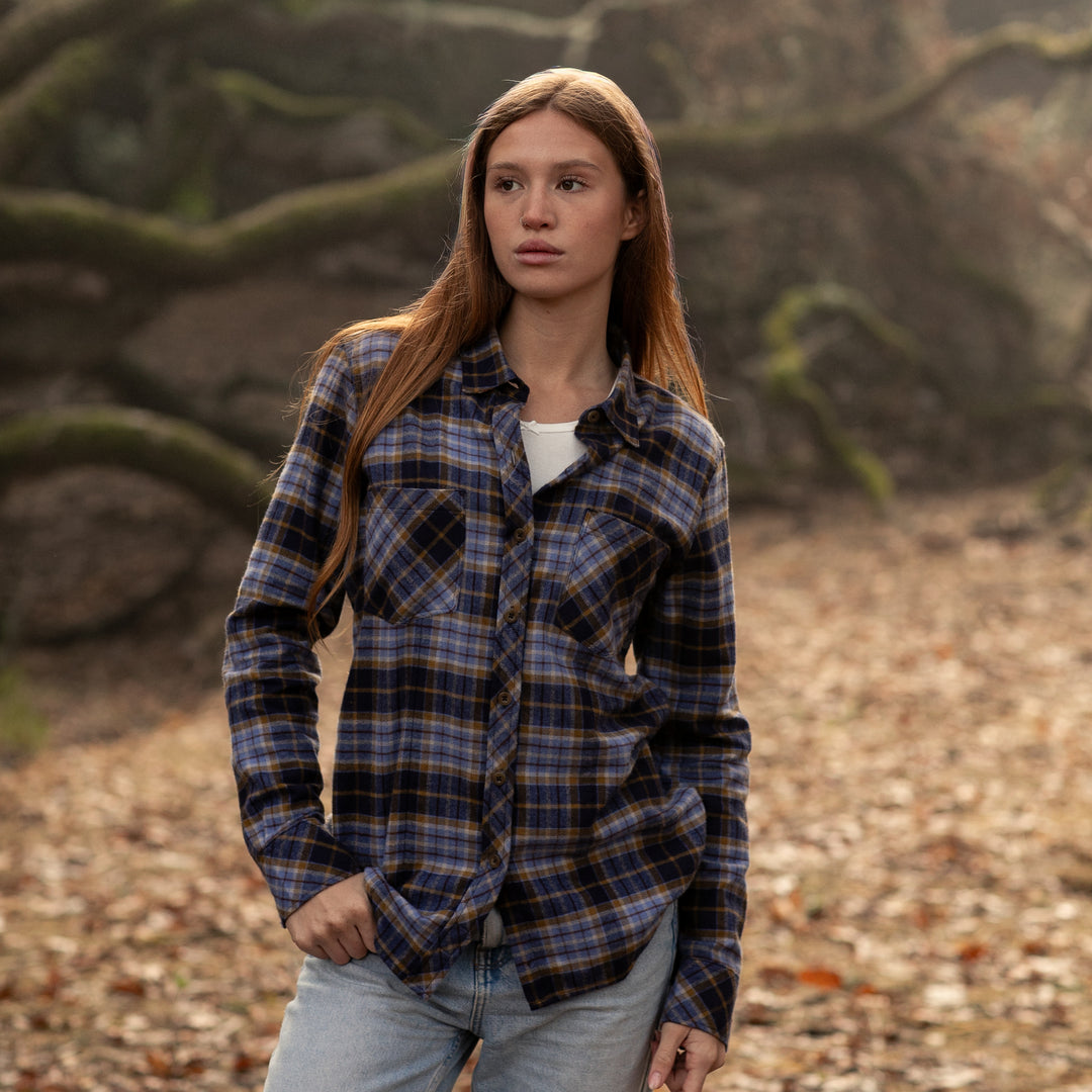Woman wearing a plaid shirt in a natural setting with trees and ground cover.